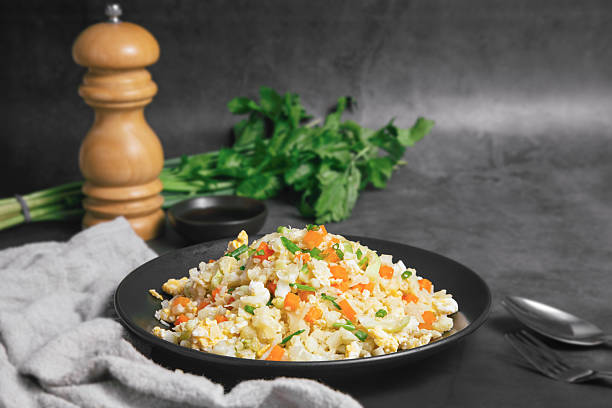 istock Non-gluten fried rice made from cauliflower, carrots and eggs, topped with spring onions. Delicious served on a plate with a black stone background. Healthy food. 2232578578