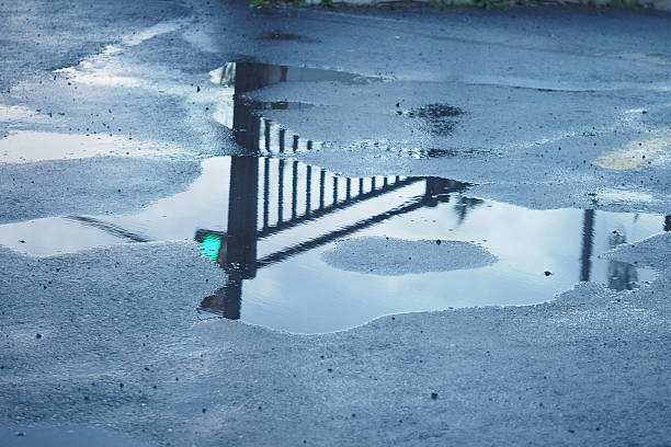 Water gathers on asphalt, mirroring a fence and green light above.