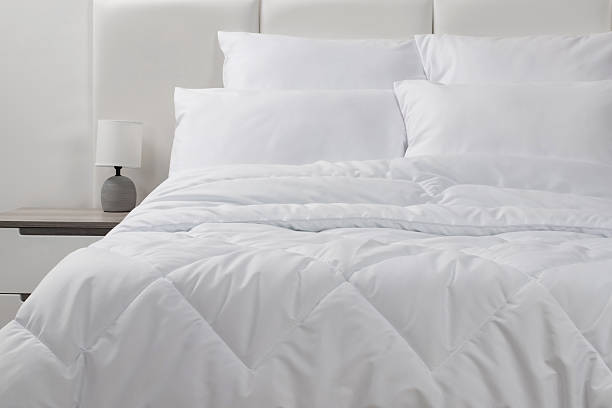 istock A bed with white pillows and a blanket, next to a bedside table with a lamp, daylight 2232590162