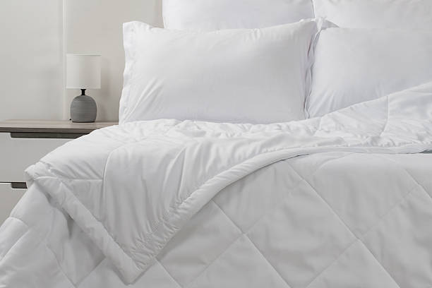istock A bed with white pillows and a blanket, next to a bedside table with a lamp, daylight 2232590163