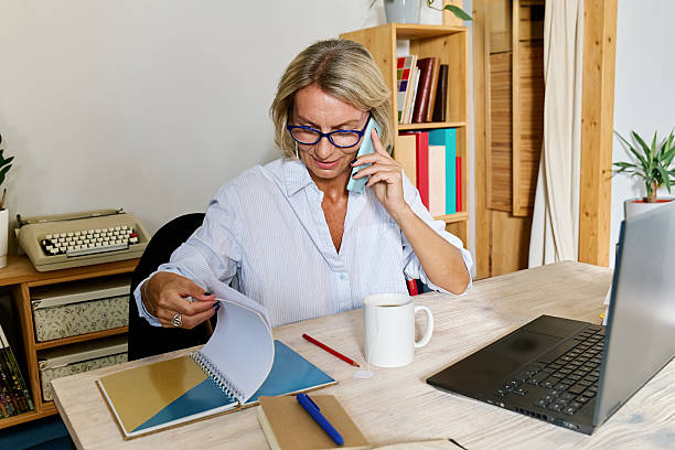 istock Smiling blond haired business woman taking notes while talking at phone in her workplace in office 2232595675