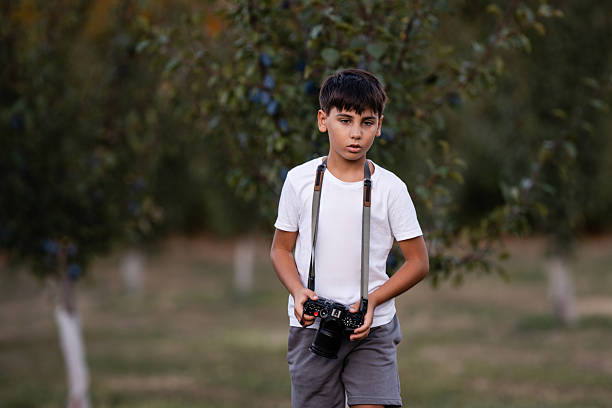 Boy holding a digital camera while wandering through a plum orchard, capturing the beauty of nature and enjoying the adventure of photography