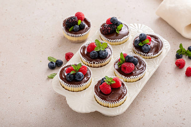 Mini cheesecakes baked in a muffin pan topped with chocolate ganache and fresh berries