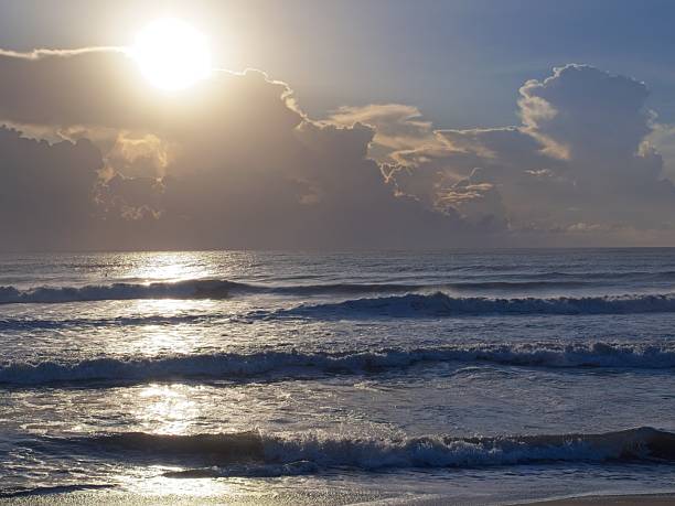 Sunlit Florida morning with ocean wave swells dwarfing thrill seeking surfers. Satellite beach waves in wake of hurricane Erin storm waves.