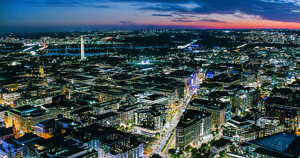 Aerial establishing shot of Washington, D.C. at night, looking over office buildings towards the Washington Monument.