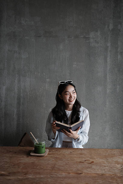 Young woman savoring a matcha latte while immersed in a book at a modern cafe, enjoying a moment of relaxation and leisure