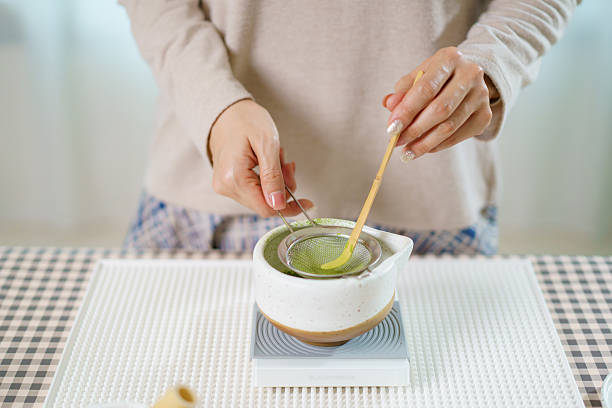 istock Asian woman preparing traditional Japanese matcha tea at home using bamboo tools, sifting matcha powder with care and precision. 2232614669