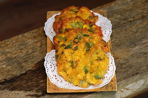 Close up of crispy Indonesian corn fritters served on a wooden plate with paper doily, traditional homemade snack.