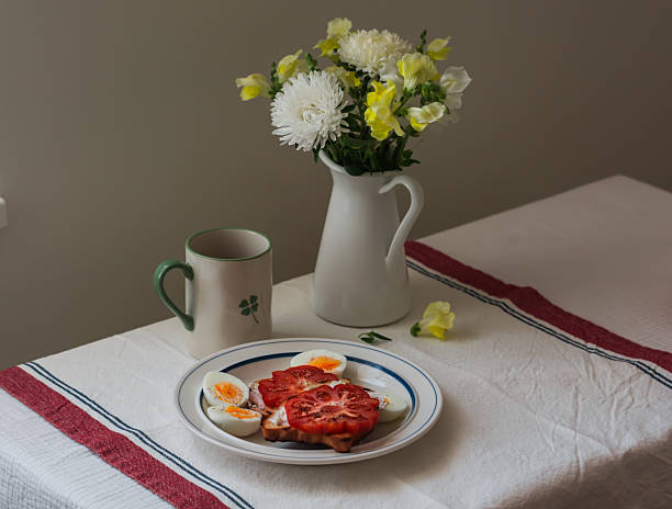 Delicious breakfast - tomatoes, cream cheese, toast, boiled eggs, coffee on the table with a bouquet of flowers
