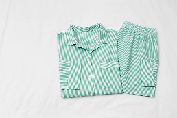 Top view of folded mint green striped pajama set on white bed. Minimal style, cozy, comfort pyjamas. Sleepwear fashion concepts, self-care, wellness, calm lifestyle, home aesthetics, morning routines