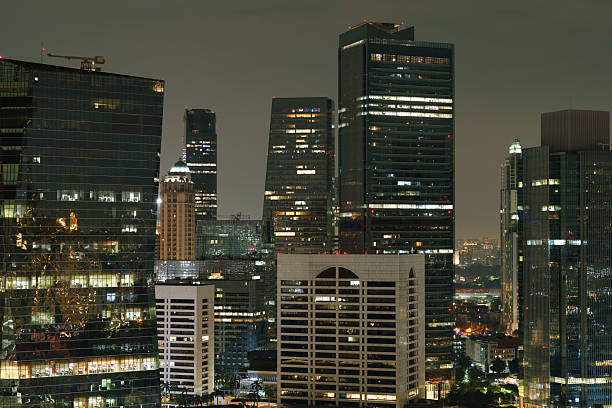Night cityscape of Jakarta, Indonesia, featuring modern downtown skyscrapers and office towers with illuminated windows. The photo captures the vibrant business district and the energy of the city at night.