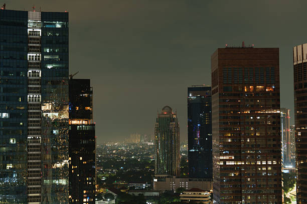 Night view of Jakarta, Indonesia, featuring modern office towers and skyscrapers with a distinctive dome-topped high-rise at the center. The illuminated buildings and city lights highlight the vibrant atmosphere and dynamic architecture of the capital at night.