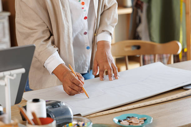 istock A woman is intently drawing a pattern on paper for a clothing design, using a pencil and a ruler to create a precise template. 2232630353