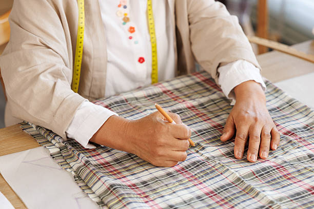 istock woman using a pencil to draw a pattern onto a plaid fabric on the table. 2232630378