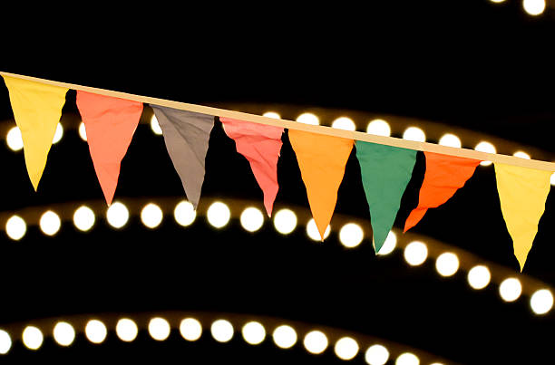 A string of flags hanging from a light fixture. The flags are of different colors and sizes. The lights are on and the flags are hanging from the ceiling