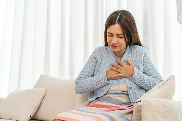 istock Young woman representing possible heart attack experiencing chest pain, placing hands over heart with distressed face sitting on sofa, heart problem, health emergency and physical discomfort 2232638140