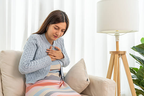 istock Young woman representing possible heart attack experiencing chest pain, placing hands over heart with distressed face sitting on sofa, heart problem, health emergency and physical discomfort 2232638143