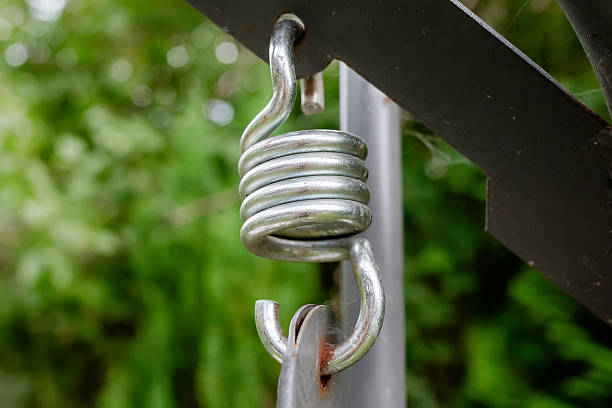 Close-up of a metal coil spring hook connected to a swing frame outdoors with blurred green background