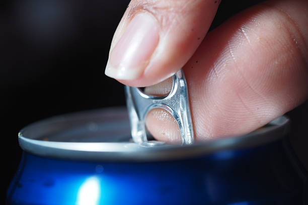 A finger pulls the tab of a blue soda can in a close-up shot.