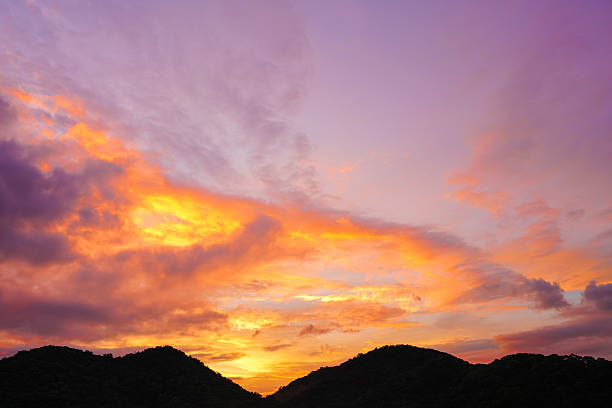 sunset sky with dramatic purple, pink, and orange clouds over silhouette mountains. Captures peaceful nature and magical twilight moment for background, travel, and nature concepts.