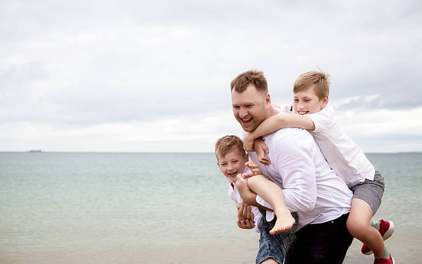 istock Dad carrying two sons on his back on the beach. Father and children having fun 2232652302