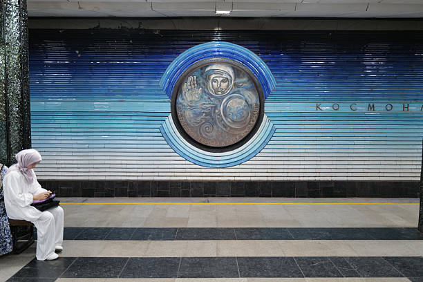 Tashkent, Uzbekistan – August 4, 2025: People wait for trains in the famous Kosmonavtlar Metro Station, a popular tourist attraction known for its spectacular space-themed design dedicated to Soviet cosmonauts, featuring blue ceramic medallions, celestial mosaics, and glass stars on the ceiling that create an immersive cosmic atmosphere. Tourists and daily commuters alike admire the unique architectural and artistic elements that make this station a cultural landmark and a must-visit destination in Tashkent.
