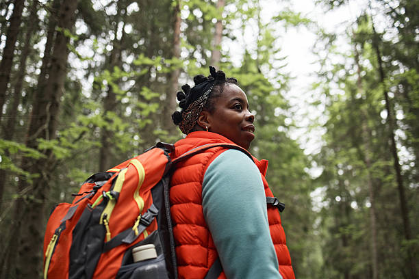 istock Middle Aged Black Woman Hiking through Forest Carrying Backpack and Looking Around 2232661482