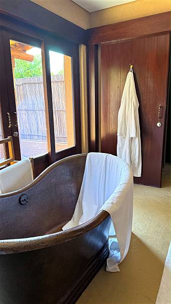 Luxurious bathroom featuring white bathrobe hanging on wooden door, white towel draping copper bathtub, conveying serene spa like ambiance