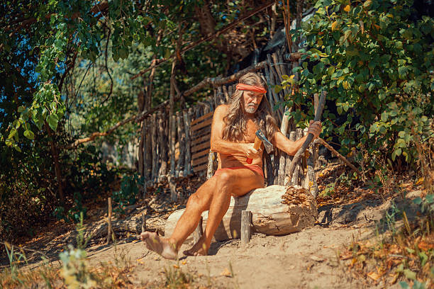 Old hermit crafting wood with a hatchet in the forest near his hut