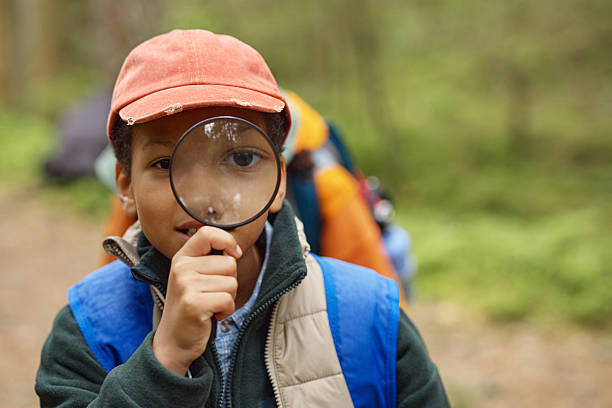 Portrait of Black Boy Exploring Nature Using Magnifying Glass Outdoors