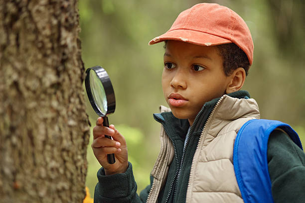 istock Curious Black Boy Examining Tree Bark with Magnifying Glass Outdoors 2232663026