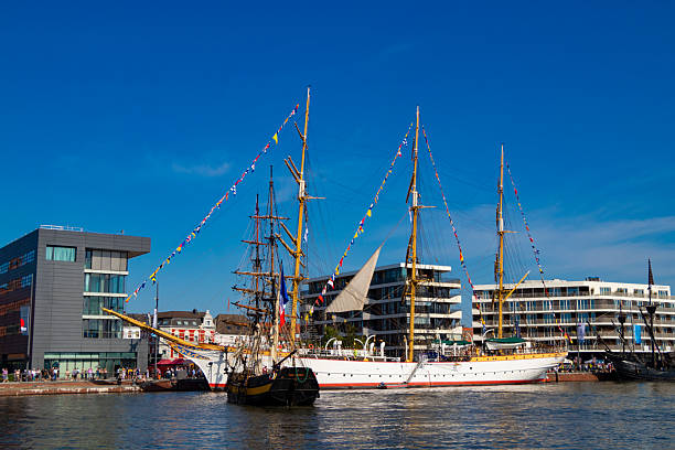 A beautiful two-masted wooden sailing ship maneuvers next to the beautiful German training ship to reach its berth at the New Harbor in central Bremerhaven, Germany, August 13, 2025