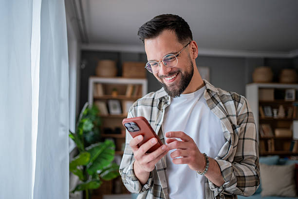 istock Smiling young man using smartphone at home reading good news 2232672988