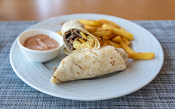 istock Delicious burrito with beef and eggs served with crispy fries and dipping sauce on a light-colored plate 2232680074