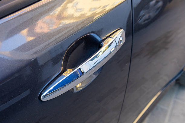 istock A shiny car door handle reflects sunlight, showcasing modern design and craftsmanship. The scene highlights urban architecture in the background 2232680075