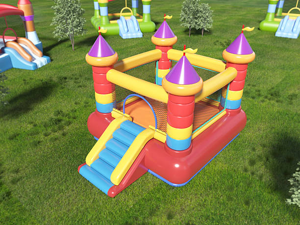 A vibrant inflatable bounce house features bright colors and castle-like towers. It sits in a grassy park alongside other play structures under a clear blue sky.