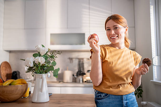 Woman holding an apple and a cookie, choosing between healthy and unhealthy food