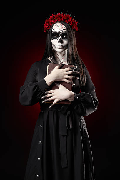 istock Young woman with calavera (sugar skull) makeup holds book (grimo 2232686508