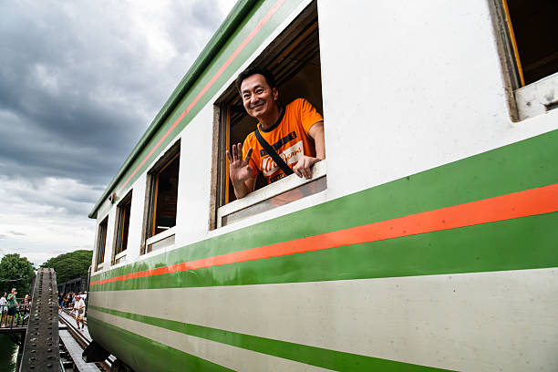 Happy Asian male backpacker waving from the train window. Transportation, people and traveling concept