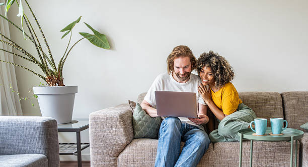istock Multiracial young couple watching computer laptop sitting on the sofa at home - Happy diverse husband and wife using pc online services - Technology life style concept 2232703462