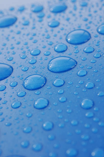 Droplets of water rest on a smooth blue surface, capturing light beautifully.