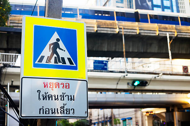 Caution pedestrian and crosswalk sign in Bangkok downtown with BTS skytrain in background