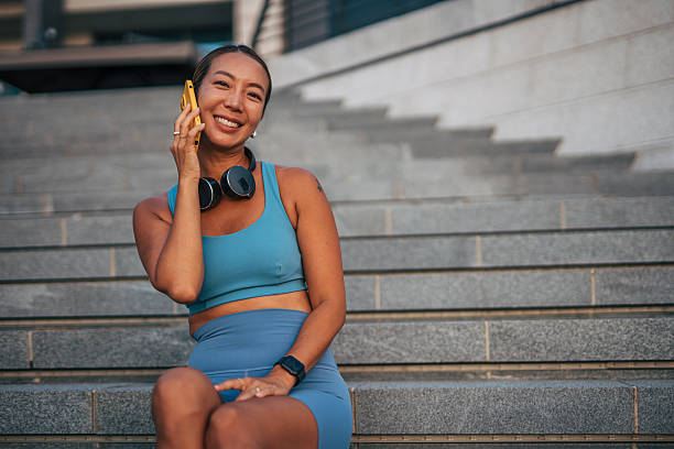 istock Smiling sportswoman making a phone call sitting on steps 2232727431