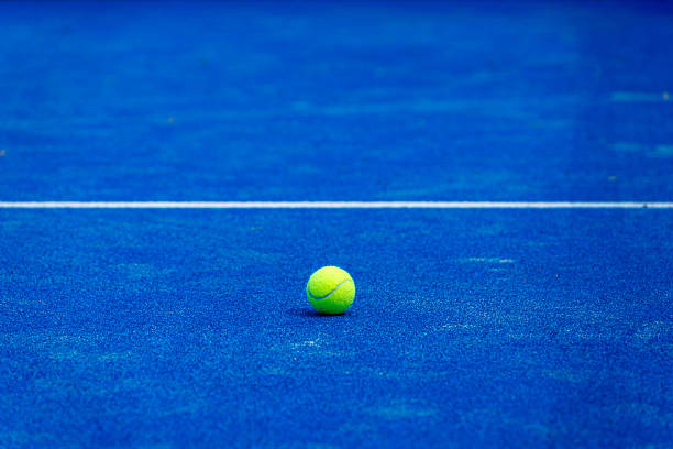 Bright yellow tennis ball on a vibrant blue paddle tennis court, ready for a serve