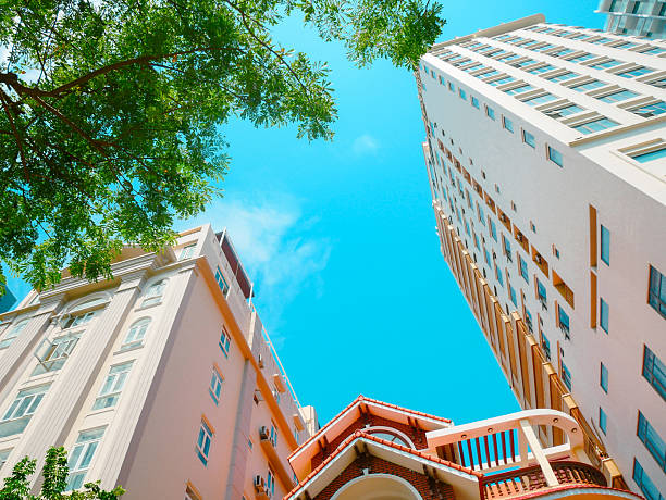 istock Festive red flags strung beneath leafy tree canopy in Danang, Vietnam. Sunlight creates lens flare beside multi-story building. Clear blue sky adds warmth to this cheerful urban moment 2232734628