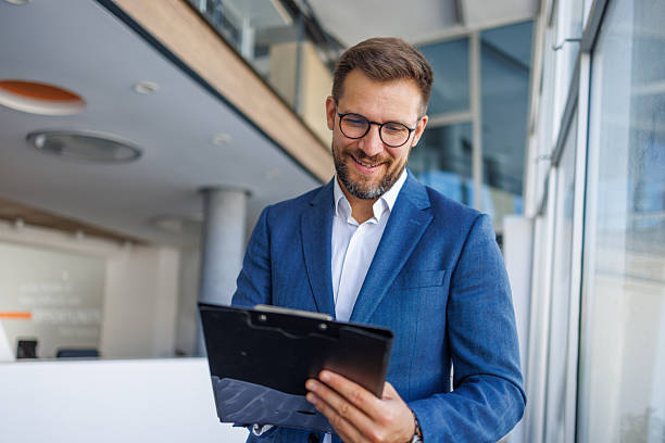 istock Smiling businessman reading notes on clipboard in office hallway 2232751785