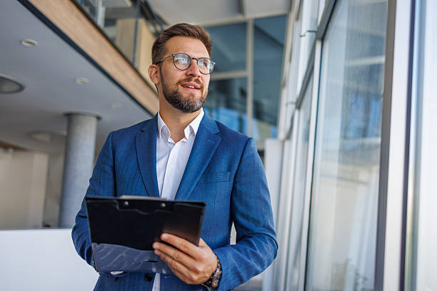 istock Businessman holding clipboard looking out office window 2232751878