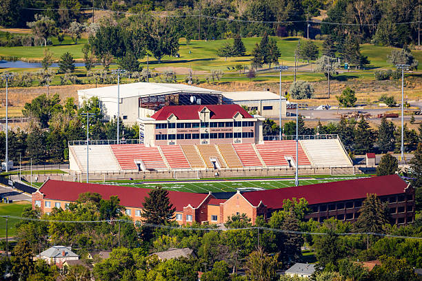 Aerial view of a sports coach talking with a collegiate track and field athlete on the football field during a training session, while in the distance the sun sets over mountains.