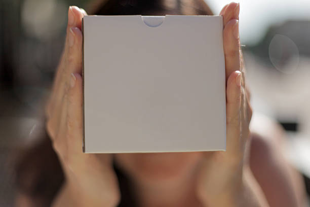 Woman holding a white box in front of her face in a sunny day