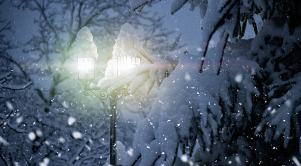 Magical winter scene featuring a glowing street lantern covered in thick snow, surrounded by snow-laden trees. Falling snowflakes add a dreamy, serene atmosphere, evoking feelings of peace, holiday spirit, and cozy winter nights. Perfect for Christmas, New Year, and seasonal backgrounds.